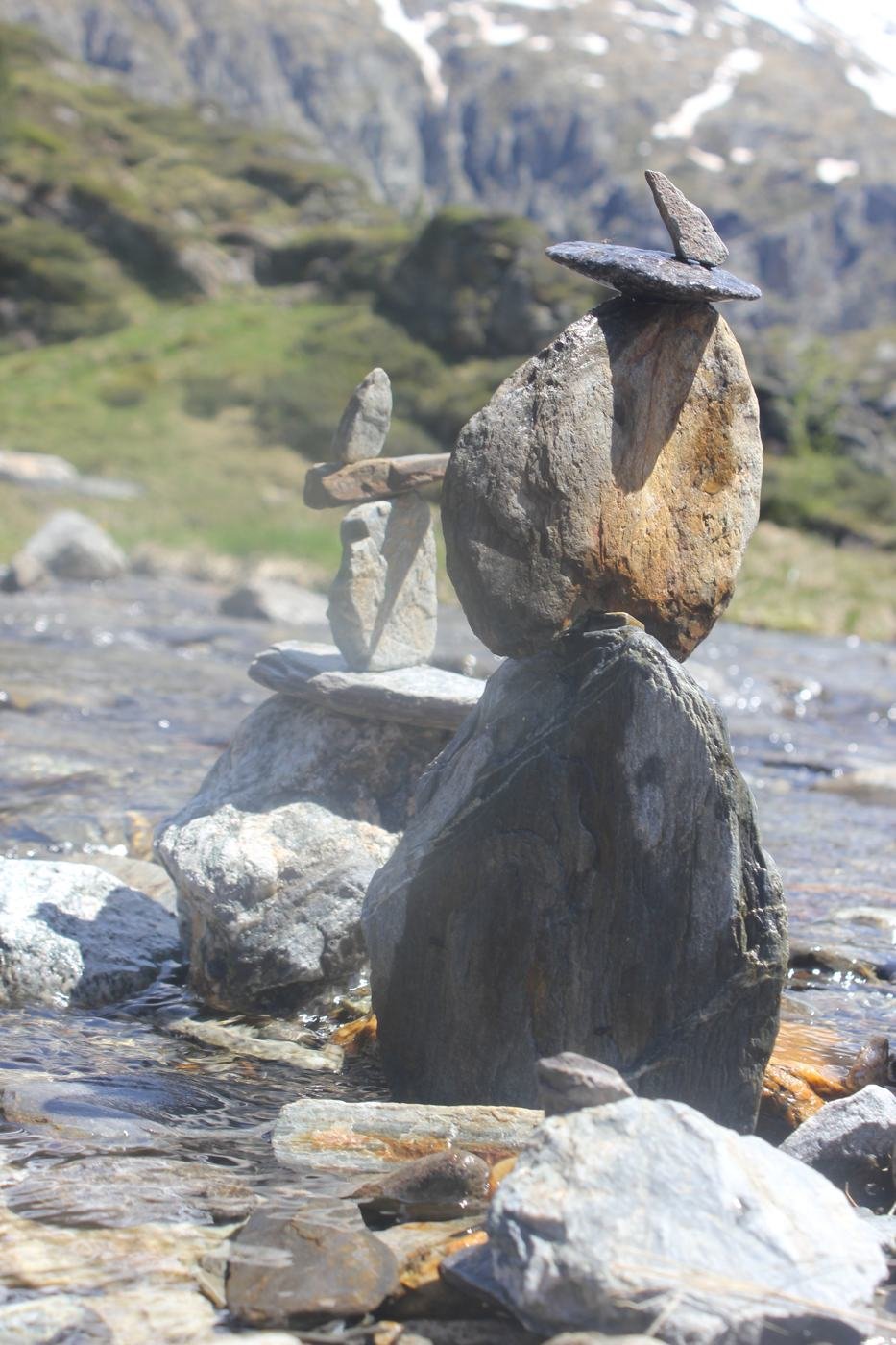 Cairn de pierres plates au bord d'un torrent, face à un sommet enneigé