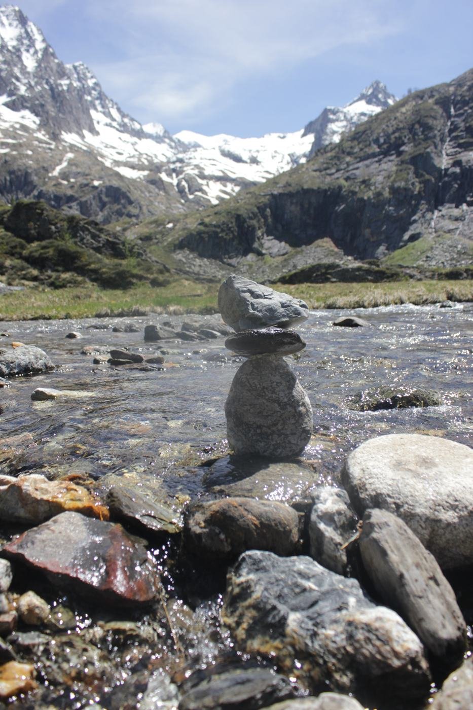 Cairn de pierres dressé dans un torrent, face aux sommets enneigés