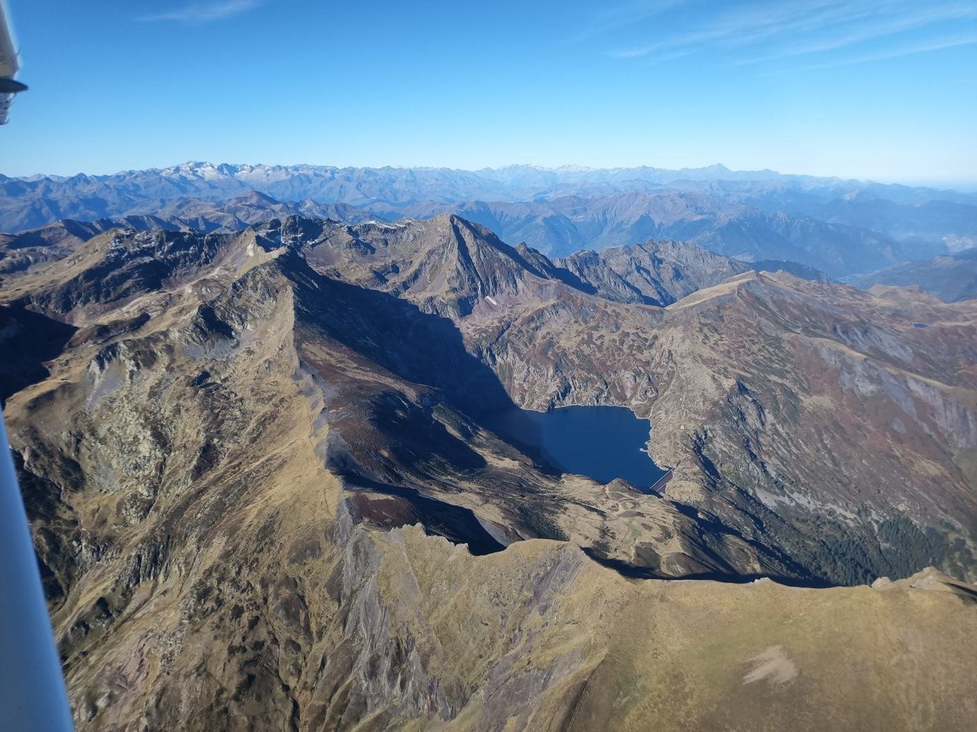 Vue d'avion sur des crêtes pyrénéennes et un lac d'altitude, bout d'aile au premier plan