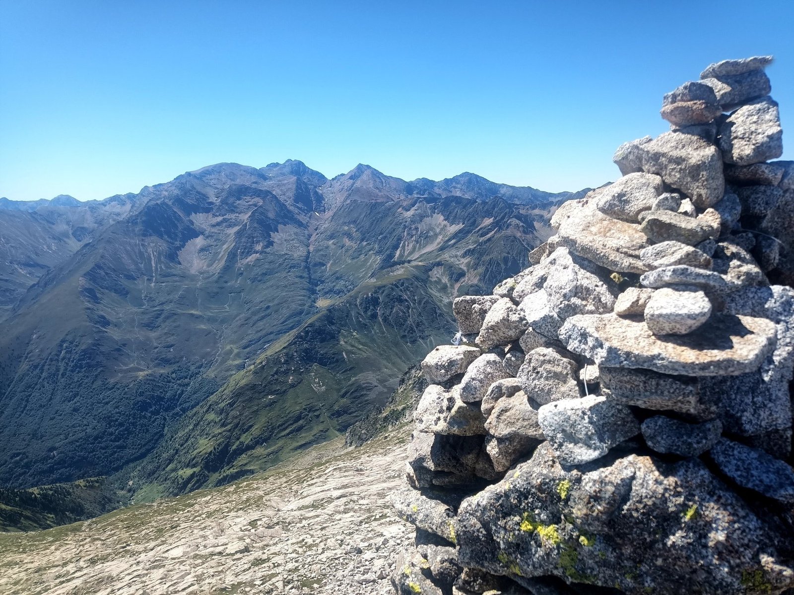 Un grand cairn de granit au sommet, face aux crêtes et aux vallées des Pyrénées