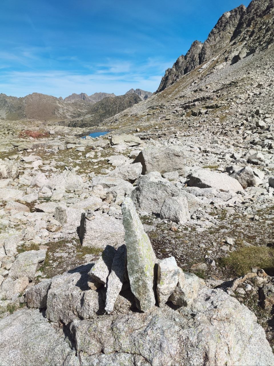 Un cairn de pierres dressées dans un chaos de granit, un petit lac au fond du vallon