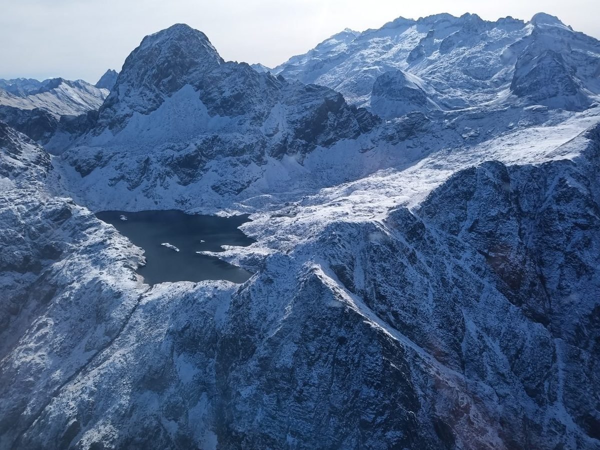 Lac d'altitude au pied d'un pic saupoudré de neige, vu d'avion