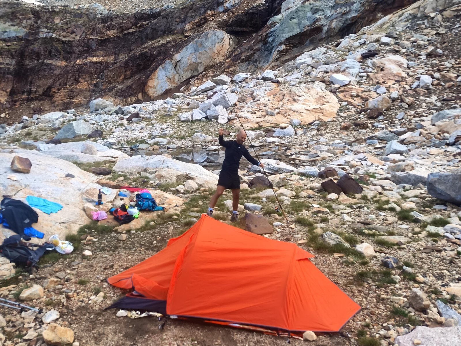 Montage du bivouac : une tente orange posée au pied d'un cirque de granit