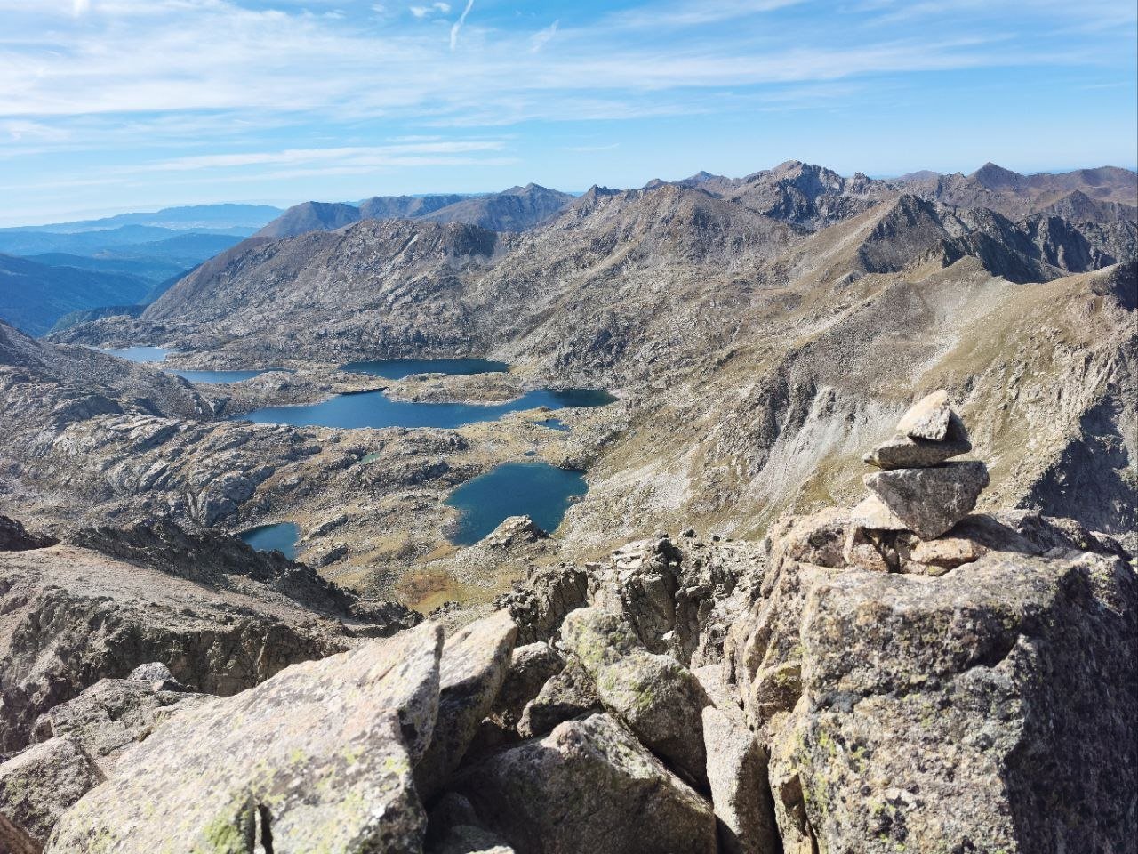 Un cairn au sommet, face à un chapelet de lacs d'altitude dans les Pyrénées