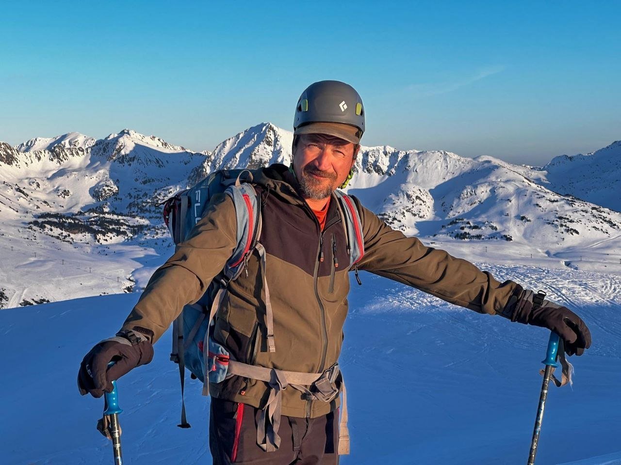 Christophe en ski de randonnée, casque et bâtons, face aux sommets enneigés dans la lumière du matin